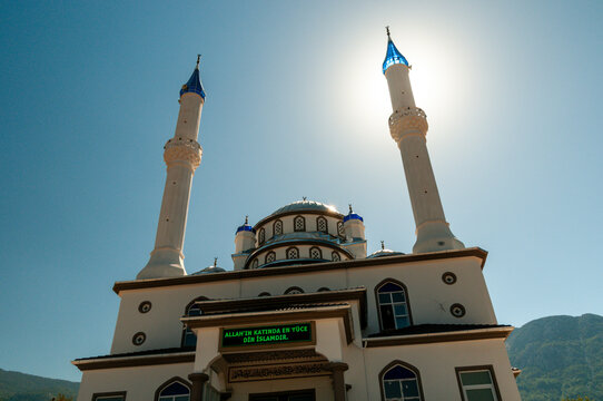 Sun behind the minaret of a Mosque displaying a message in Turkish "The most high religion in Allah is Islam"