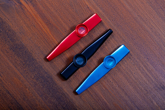 Three kazoos red, black, and blue on a wooden surface. Simple musical instrument. Music education or fun activity for child
