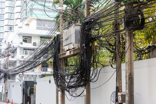 Messy and untidy electrical cables hanging from an electricity pole in Thailand