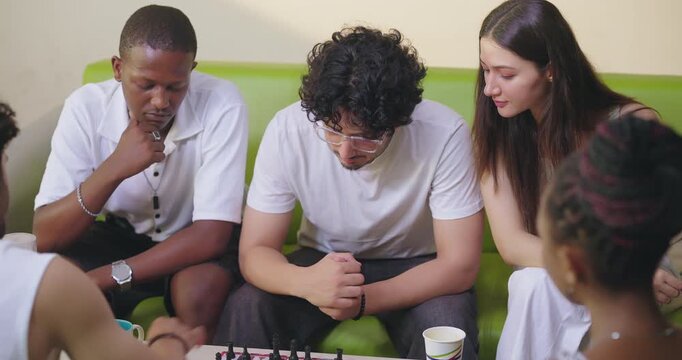 Indian young adult gen z male female group team sitting on sofa couch play chess indoor room place teen girl boy look game watch match talk speak share idea spend break time enjoy new day have fun joy
