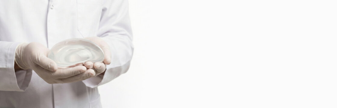 Plastic surgeon holds breast augmentation implant in hands in front of him. Close-up of doctor's hands with implant for medical mammoplasty. White background. Free space on right