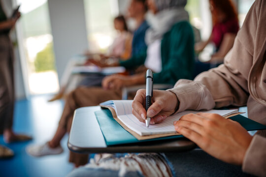 Close up of college student writing notes during lecture.