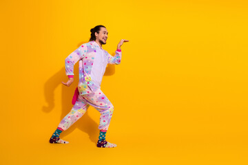 Naklejka premium Playful man in colorful unicorn pajama jumpsuit dancing in bright yellow studio home lifestyle image