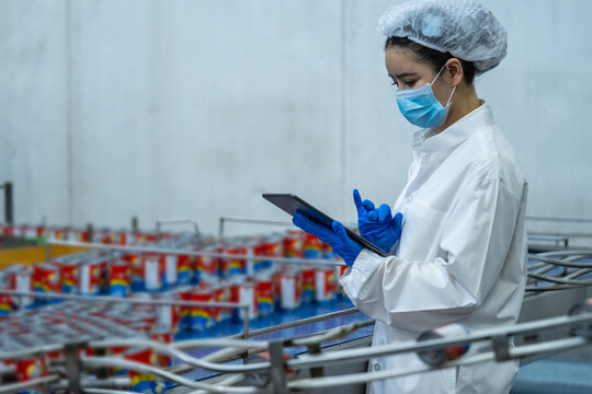 Quality assurance inspector entering data on tablet beside canned food conveyor
