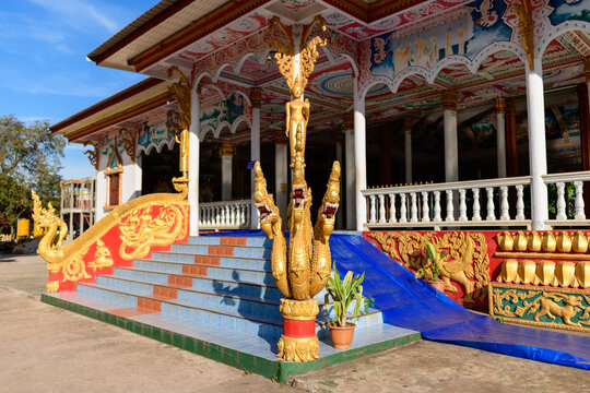 Golden multi-headed naga statue decorates the colorful entrance steps of a traditional Buddhist temple in Vientiane, Laos. Intricate carvings, vibrant murals, and detailed architectural elements are