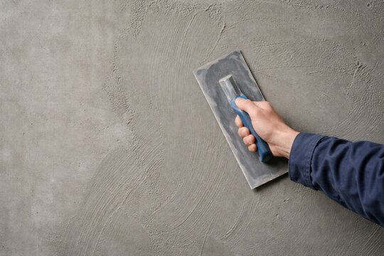 Male worker hand holding a trowel and plastering gray concrete wall.