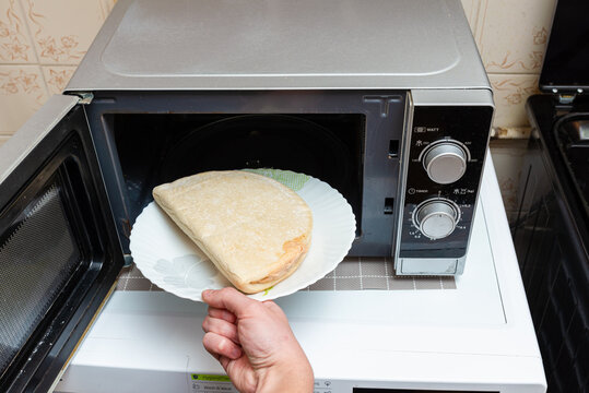 Unhealthy food, fast food, junk food concept. Unprocessed fast food unhealthy small frozen pizza placed in boy's hand while being put in microwave.