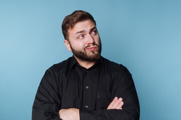 Obraz premium Confident man displays playful curiosity with crossed arms against a vibrant blue background during a relaxed moment of reflection