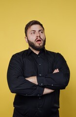 Obraz premium Surprised man with crossed arms expresses curiosity against a bold yellow backdrop in a casual setting