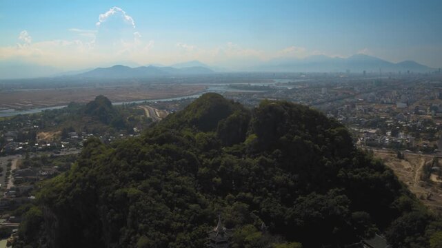 Aerial drone view flying around the marble mountains with a pagoda and da nang city in the background