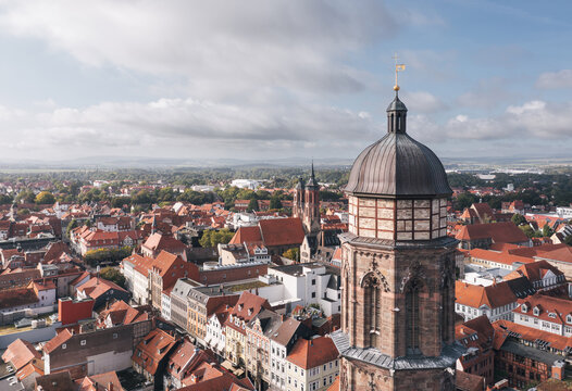 Close drone view over Goettingen (G&ouml;ttingen), Germany, highlighting a historic tower above red roofs and the surrounding cityscape, with soft clouds and open sky providing copy space.