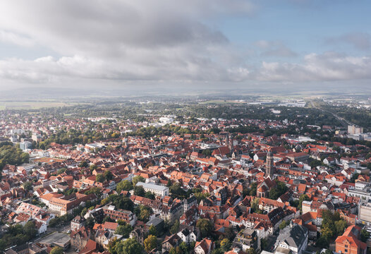 Wide drone panorama of Goettingen (G&ouml;ttingen) in Lower Saxony, Germany, showing the historic city center with red roofs, church towers, and surrounding green landscape under a dramatic cloudy sky.