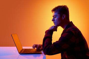 Side view of man analyzing information on laptop in modern neon studio setting. Concept of data...