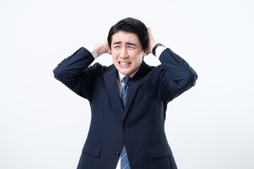 頭を抱えるスーツを着たビジネスマン　困るやミスや失敗などのイメージ　白背景