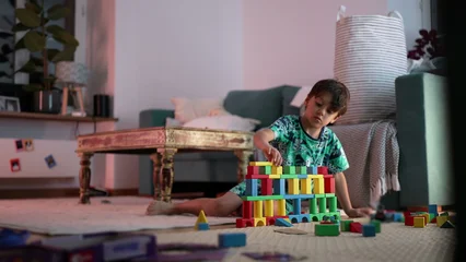 Fotobehang Lego Young boy building colorful block tower, focused on creativity and play in cozy living room setting, sitting on mat surrounded by scattered toys and blocks  © Marco