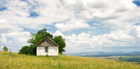 A lonely house on a mountaintop. Summer landscape with a small hut in the mountains. Clouds in the sky. Fields are visible in the valley in the distance. Beautiful panorama. Krasnodar Krai, Russia.