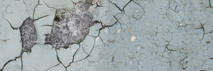 Peeling paint on the wall. Panorama of a concrete wall with old cracked flaking paint. Weathered rough painted surface with patterns of cracks and peeling. Grunge texture for wide panoramic background