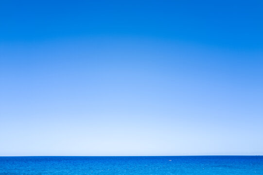 A seamless gradient of blue sky meets the tranquil Mediterranean Sea in a minimalist seascape near Cala Goloritze, Baunei, Sardinia. The scene radiates calm and simplicity, with no land or objects