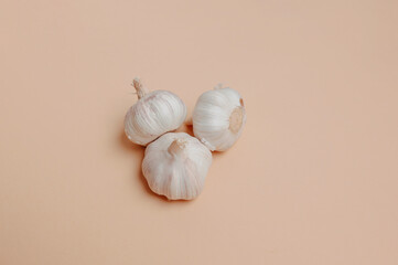Display Of Three Raw Garlic Bulbs In Triangle Layout Over Peach Surface Highlighting Organic Texture