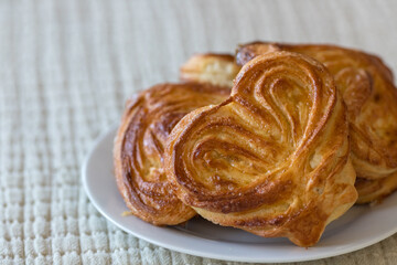 Fototapeta premium Golden brown sweet bun on a plate. Freshly baked yeast dough pastry. Heart-shaped puff pastry with sugar