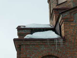 Melting snow and icicles hanging down from a brick building cornice. Winter weather and seasonal architectural detail. © Olesia Basova
