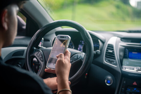 Person using mobile phone and texting while driving, creating a dangerous road safety hazard.