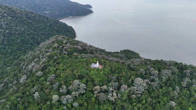 Aerial shot shows Muka Head Lighthouse overlooking turquoise sea with dense tropical forest backdrop.