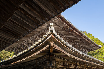 Fototapeta premium Close-up view of intersecting temple eaves at Engyoji, Mount Shosha, Himeji, Japan, showcasing elaborate wooden craftsmanship and decorative roof tiles under a clear sky. Sunlight highlights the