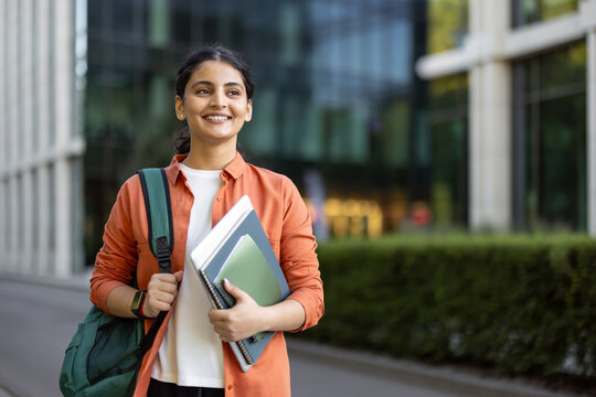 Happy indian student carrying a backpack and notebooks, confidently walking on a university campus, representing education, success, and future career aspirations