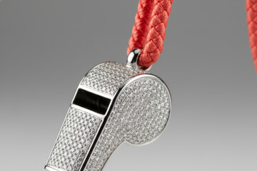 Luxury silver whistle encrusted with diamonds hanging on red cord illustrating premium sports referee gear, championship coaching awards and expensive game authority concepts