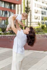 Obraz premium Happy Mother Lifting Baby in Air Outdoors in Modern Residential Neighborhood