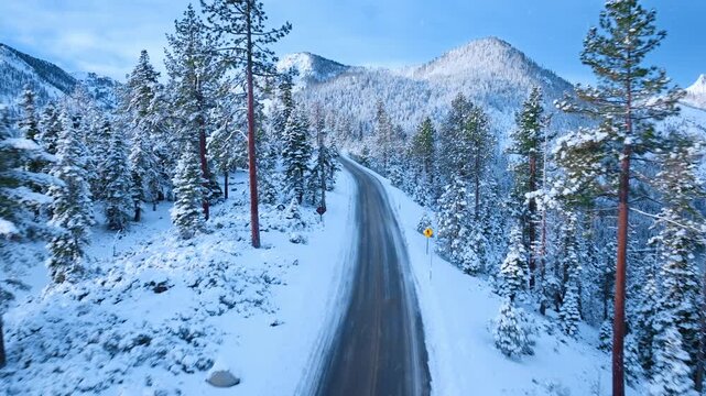 Golden sunrise illuminating Emerald Bay Road along snow covered mountain ridge above Lake Tahoe. Warm morning light contrasts with frozen pine forest creating dramatic alpine winter scenery.