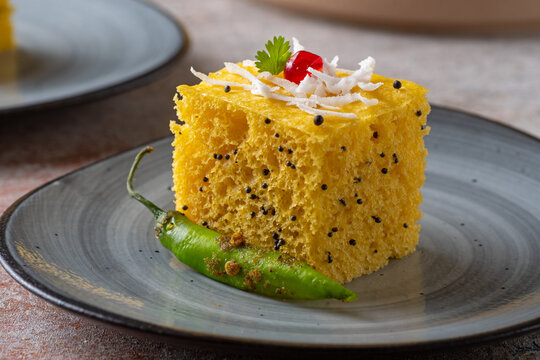Gujarati Khaman Dhokla with Mustard Seeds and Green Chilli &ndash; Soft Nylon Dhokla Garnished with Coconut and Pomegranate seed on Ceramic Plate