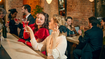 Obraz premium Women enjoying martinis at bar counter in retro evening setting. Concept of cocktail culture promotion, mixology workshop advertising and stylish nightlife content creation.