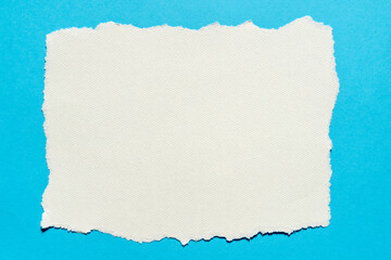 Obraz premium Torn piece of white textured paper on a blue background