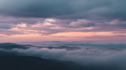 Obraz premium Serene mountain range at dawn with soft pastel sky and atmospheric mist filling the valleys under a dramatic cloudscape