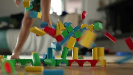 Fototapete Lego Wooden block structure collapsing as young boy's leg kicks it during playtime, colorful blocks tumbling onto floor in dynamic motion, playful indoor activity and creative fun  © Marco
