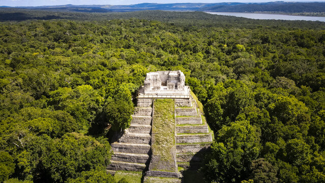 Aerial view of the ancient Mayan temple soaring above the lush green jungle canopy, with a distant lake shimmering under the sun, Guatemala, Guatemala, Guatemala.