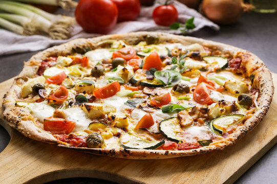 Fresh vegetarian pizza with mozzarella, tomatoes and zucchini on wooden board
