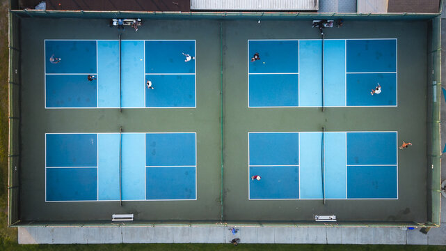 Aerial view of vibrant blue pickleball courts contrasting against the surrounding green, capturing the energy of players in motion, Coronado, California, United States.