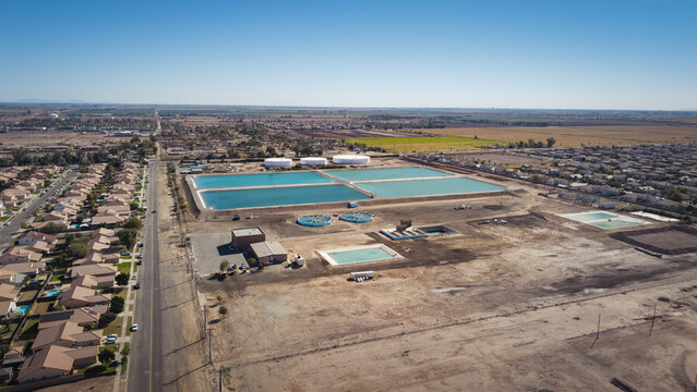 Aerial view of shimmering turquoise water treatment ponds contrasting with the arid landscape and residential areas, El Centro, California, United States.