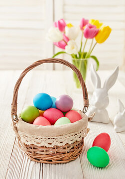 Easter basket with dyed eggs and tulips on wooden table