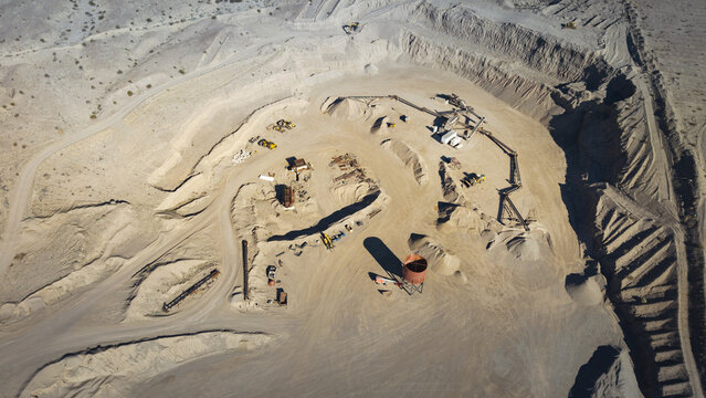 Aerial view of a sun-baked, ochre-toned landscape scarred by heavy machinery and excavation, where rust-colored equipment contrasts against the pale earth, Ocotillo, California, United States.