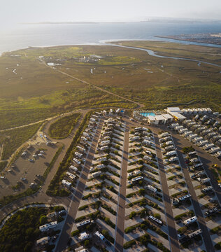 Aerial view of neat rows of RVs parked in a sun-drenched park, a contrast to the wild, green landscape and the calm ocean beyond, San Diego, California, United States.
