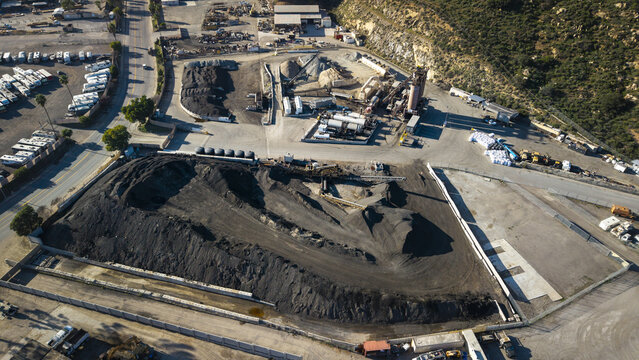 Aerial view of a large black mound contrasting with the surrounding beige landscape and industrial structures, Lakeside, California, United States.