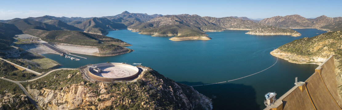 Aerial view of a vibrant blue lake reflecting the clear sky, surrounded by rugged mountains and a unique circular structure, Lakeside, California, United States.