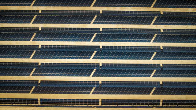 Aerial view of vast solar panel array stretching across the arid landscape, creating a geometric pattern of light and shadow, El Centro, California, United States.
