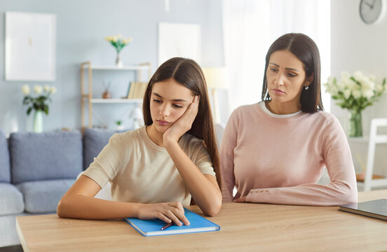 Sad teenager under stress in need of mothers help and calm support. Daughter and mom talk about problems at school and relationships with friends, teen and woman sitting at home table and talking