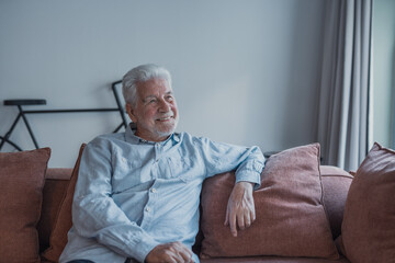 Fototapeta premium A senior man relaxes on a comfortable couch while gazing through the window, embracing serenity and thoughtful reflection during a tranquil moment in his home environment