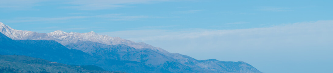 Fototapeta premium Chilly mountain ridges stand under a vast light blue sky. Pristine snowy peaks in distant haze create a fresh wintry landscape with wide airy space for modern design